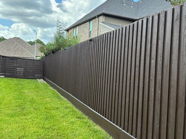 Modern dark brown wood fence bordering a green lawn and houses. Contemporary fence design.