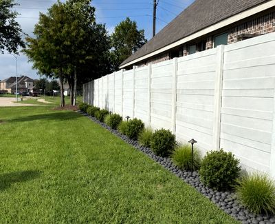 Neatly landscaped backyard with bushes, stones and white fence.