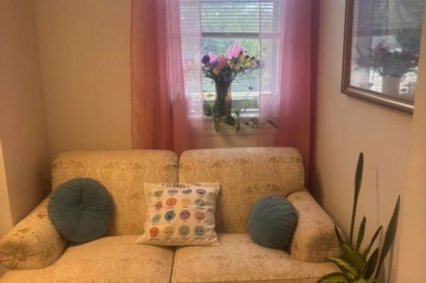 Cozy beige couch with decorative pillows and flowers by window.
