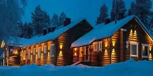 Snow-covered cabin warmly lit at night.