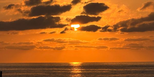 Orange sunset over calm ocean with scattered clouds.
