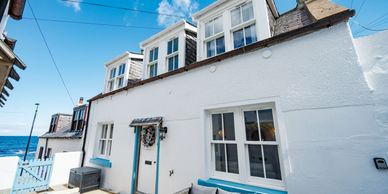 White seaside cottage with blue accents and outdoor seating under a clear sky.