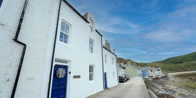 Coastal white houses with blue doors along a seaside path under a clear sky.