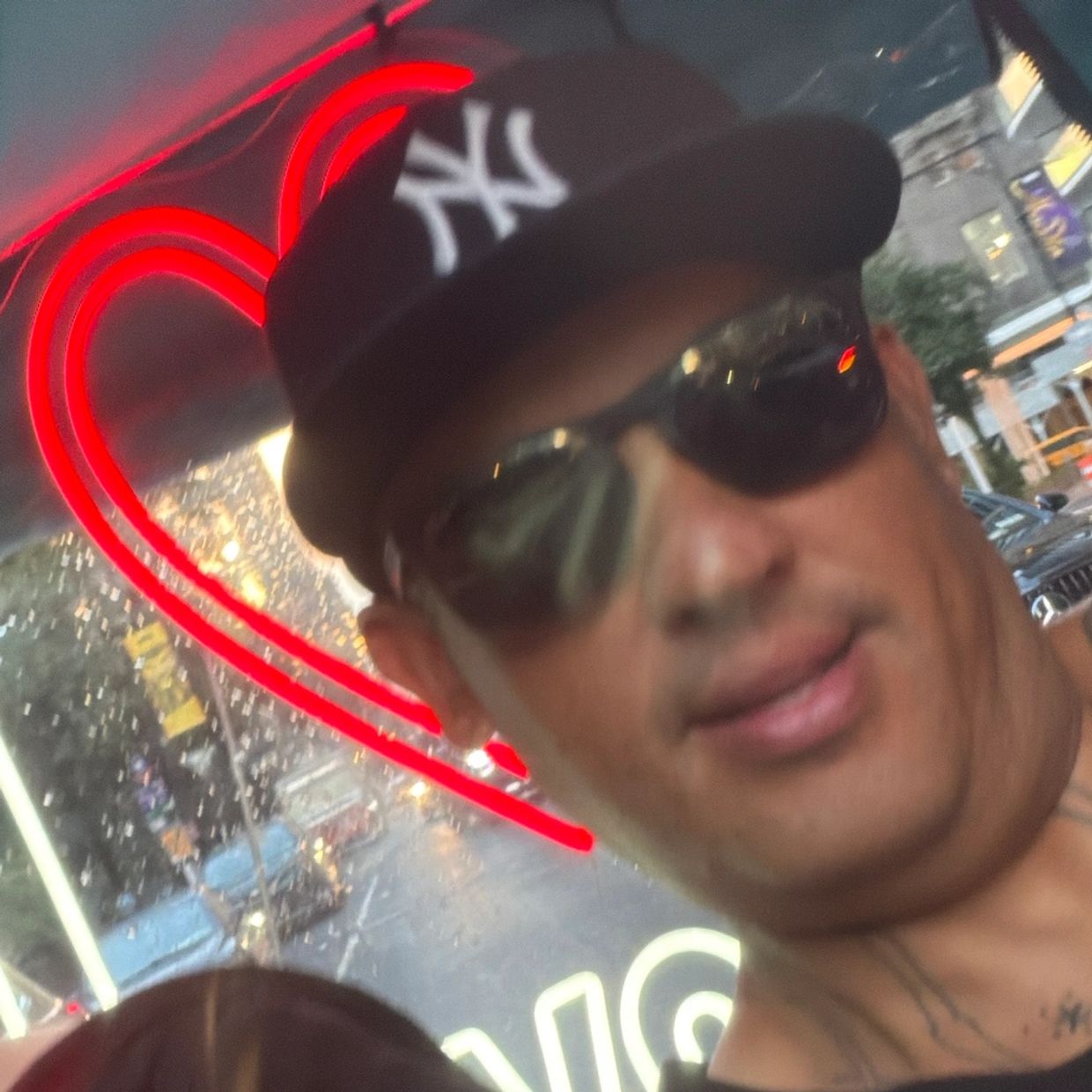 Man wearing sunglasses and a New York Yankees cap with a red neon heart behind.