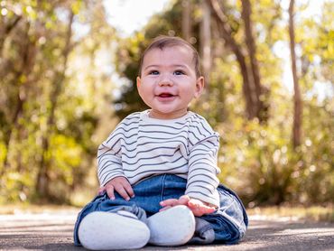 Smiling baby sitting outdoors on a sunny day.