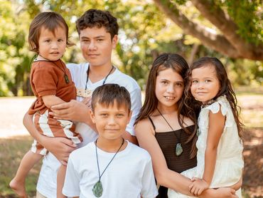 Five children posing outdoors with smiles and natural greenery in the background.