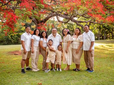 A family of nine posing under a vibrant red-flowered tree in a park.