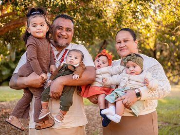 A happy family of six posing outdoors with autumn trees in the background.
