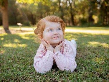 A red-haired girl lies on grass, smiling and looking up.