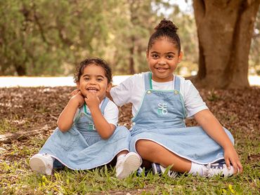 Two happy sisters in matching blue dresses sitting on grass outdoors.