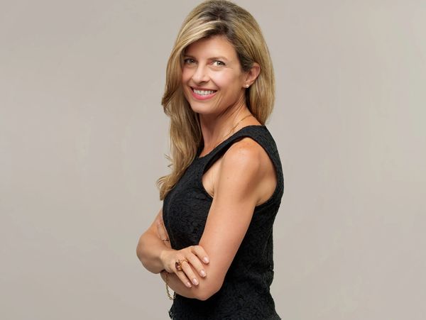 Confident woman with blonde hair smiling, wearing a sleeveless black top.