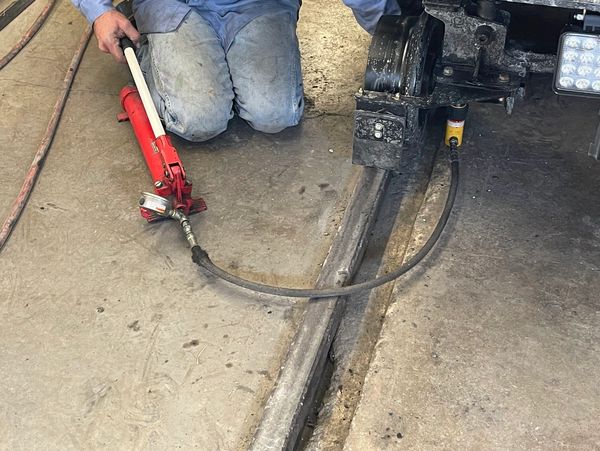 Person using a hydraulic jack to lift a heavy vehicle or machinery.