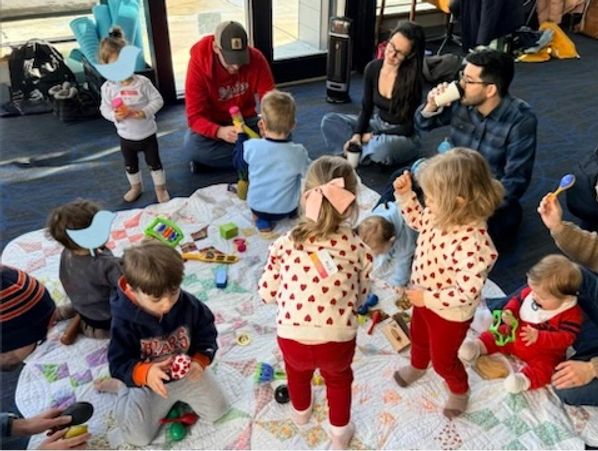 Children and adults engaged in a group activity on a blanket indoors.