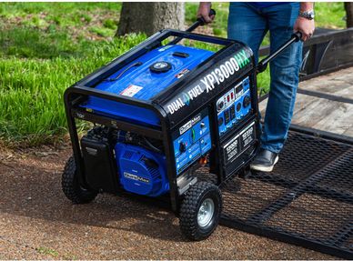 Person maneuvering a blue DuroMax XP13000HX dual fuel generator outdoors.