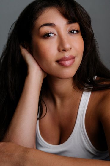 Young woman with natural makeup and a white tank top.