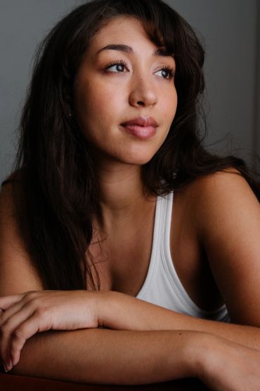 Young woman in white tank top looking thoughtful.