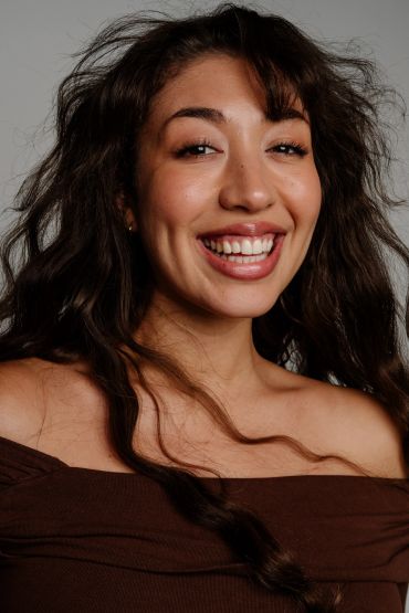 Happy woman smiling with natural hair and off-shoulder brown top.