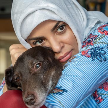 Woman in white hijab cuddling a brown dog with affection.