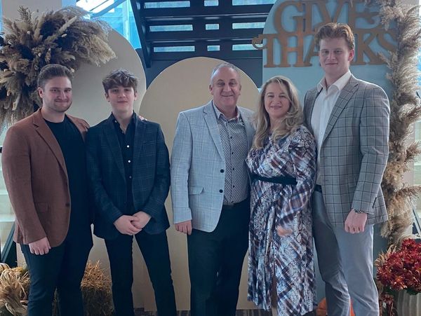 Family dressed formally posing under a staircase with a 'Give Thanks' sign.