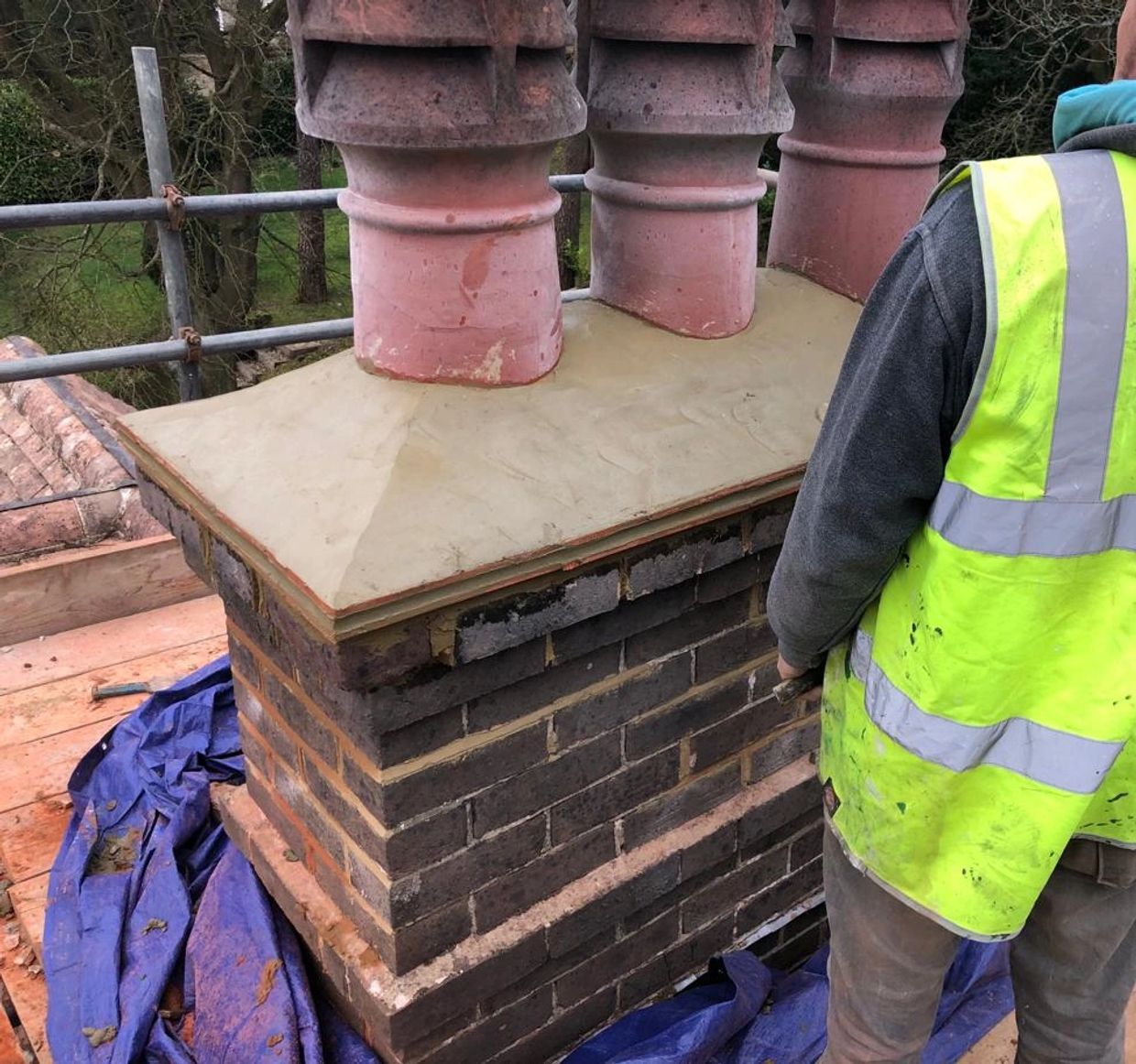 Worker in high-visibility vest near newly constructed brick chimney with clay pots.