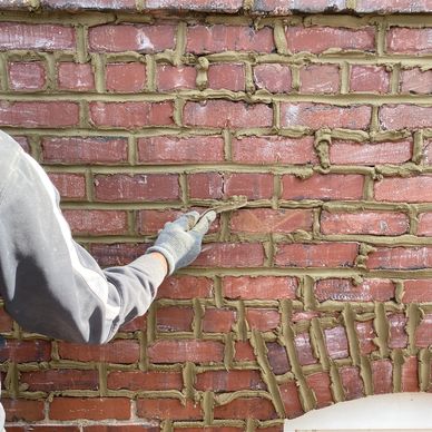 Person applying mortar to a brick wall with a gloved hand.