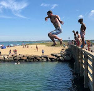 A boy jumps off a pier into the water on a sunny beach day.