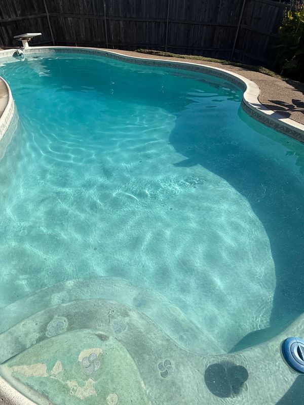Clear swimming pool with visible steps and a diving board in a backyard.