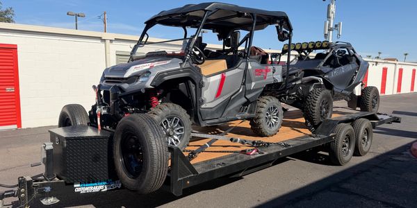 Two off-road vehicles loaded on a trailer outside storage units.