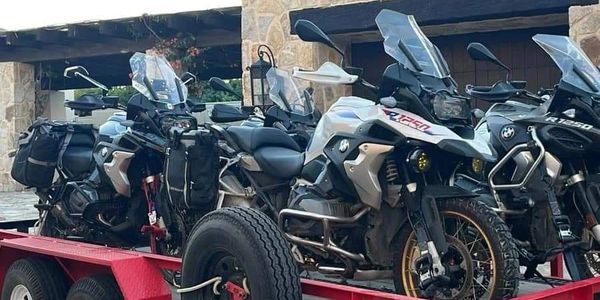 Three BMW adventure motorcycles on a red trailer.