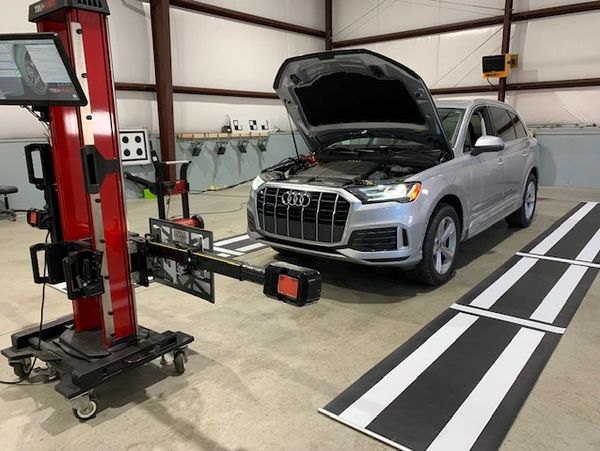 Silver Audi SUV with open hood in a garage near diagnostic equipment.