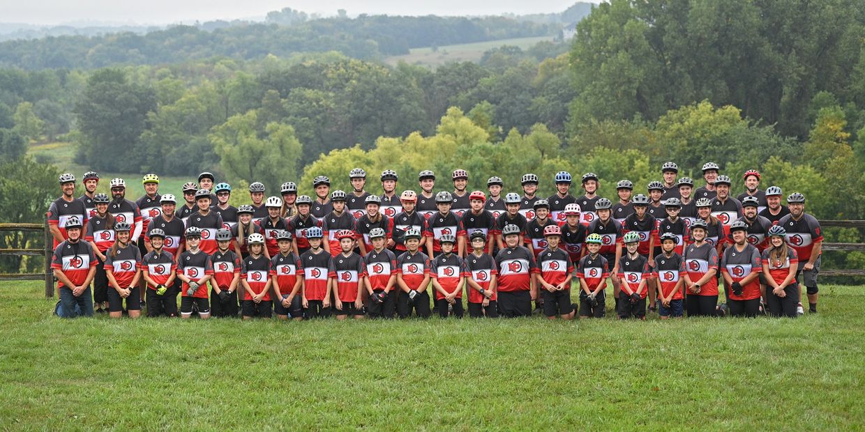 Large group of cyclists posing outdoors in matching gear and helmets.