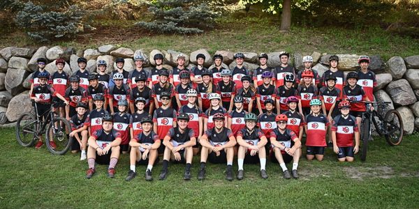 A large group of cyclists in matching uniforms posing together outdoors.