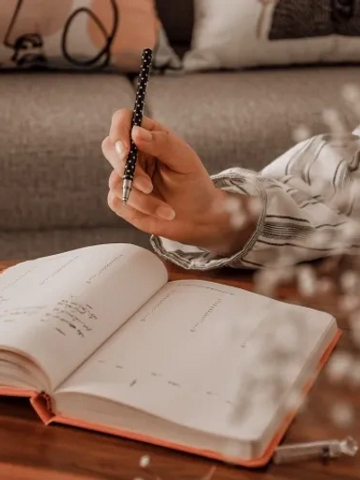 Woman holding a black pen over a journal, taking a break from writing.