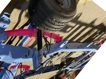 Partially assembled vehicle frame with blue chassis and pink leaf springs in a workshop.