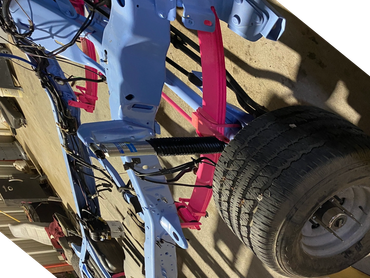 Partially assembled vehicle frame with blue chassis and pink leaf springs in a workshop.