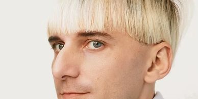 Close-up of a man with a unique blonde haircut and light blue eyes.
