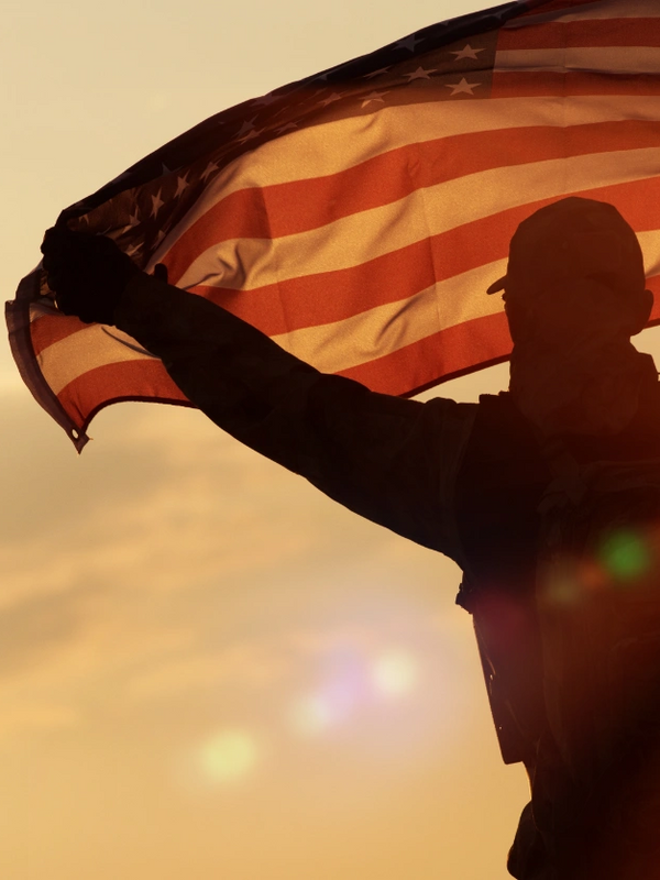 US Amry Soldier holding the American Flag outside with the wind blowing  and sun shining through