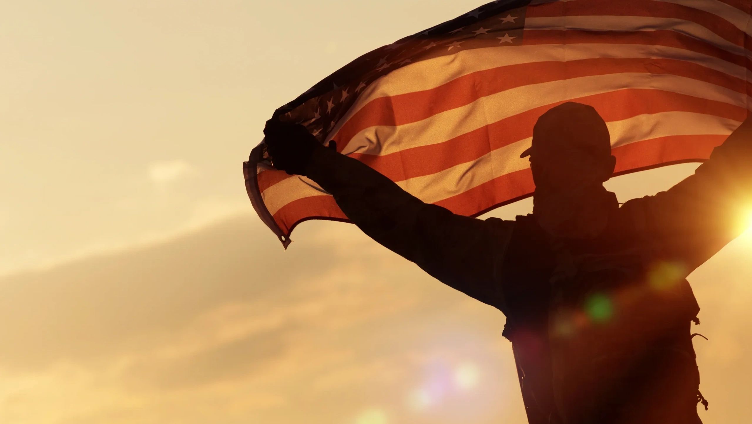 A soldier holding an American flag over his head, and the wind blowing it
