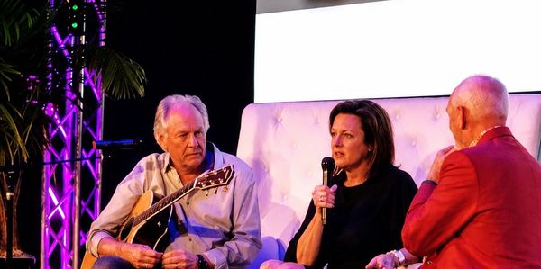 Three people engaged in a discussion, one holding a guitar.