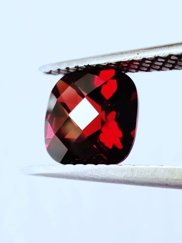 Close-up of a red gemstone held by tweezers.