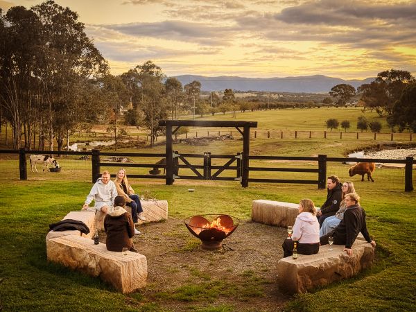Guests enjoying a drink of wine sitting around an open fire with the fam animals grazing nearby in t