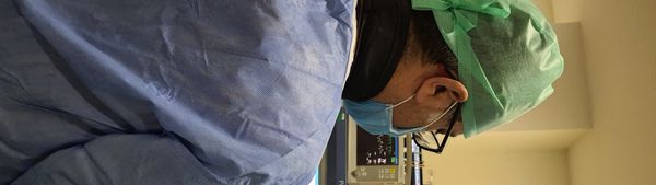 Medical professional in scrubs and mask working with monitoring equipment.