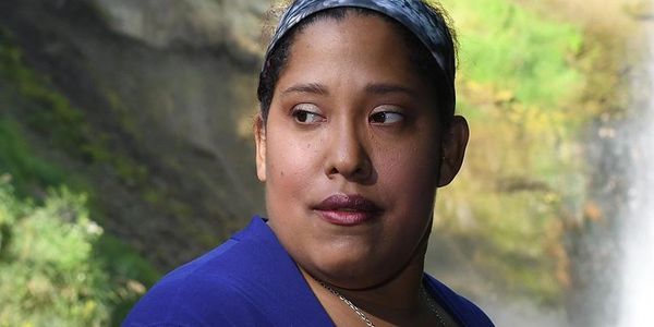 Nyleve Eiram of Nyleve Speaks Bold standing confidently near a waterfall wearing a blue top. A proud brain tumor survivor and advocate, she embodies resilience, healing, and bold truth telling.