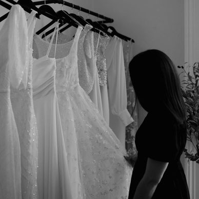 Woman viewing white dresses on hangers.