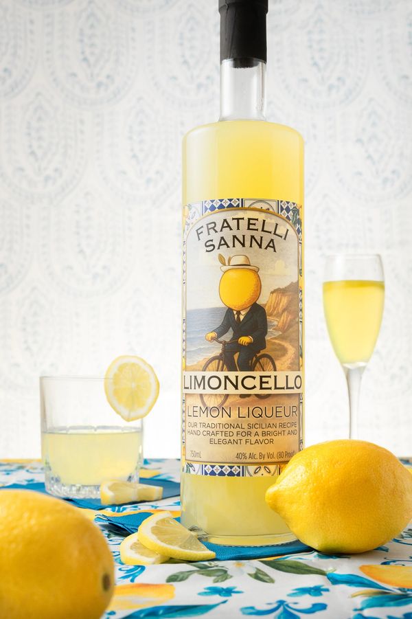 Bottle of Fratelli Sanna Limoncello with lemons and glasses on a colorful tablecloth.