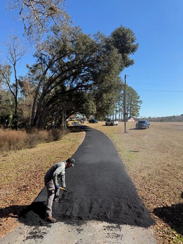 Worker paving a winding path with fresh asphalt on a clear day.