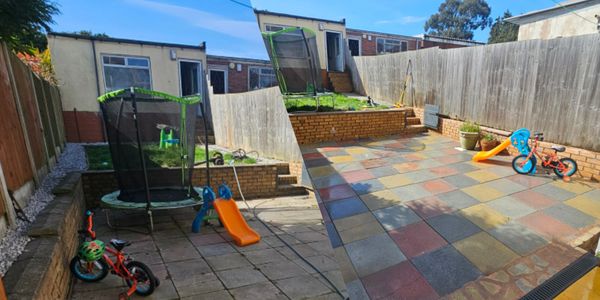 Before and after photos of a backyard makeover with colorful tiles replacing old concrete slabs.