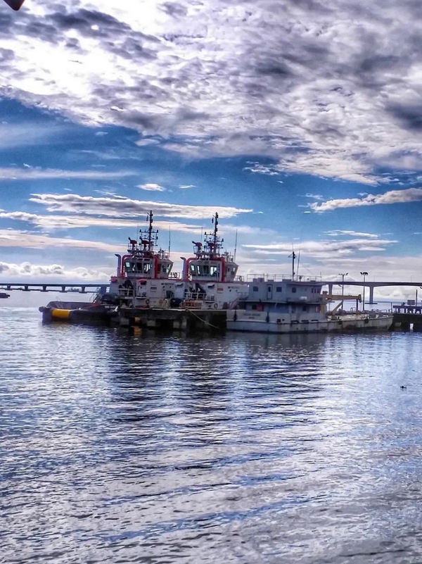 Two tugboats docked on calm waters under a partly cloudy sky.