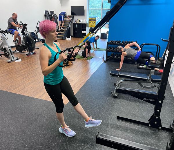 Woman with pink hair using suspension straps in a gym workout.