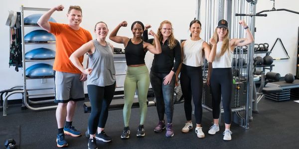 Group of six people flexing muscles in a gym setting.